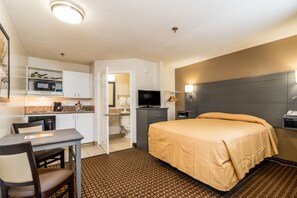 Een hotelkamer met een bed, een bureau met stoel, een magnetron, een televisie en een badkamer, zichtbaar door een geopende deur.