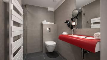 A modern bathroom with a toilet, a sink with a red countertop, a mirror, and a towel dispenser.