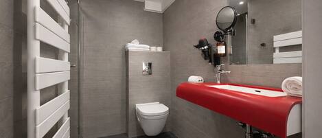 Une salle de bain moderne équipée de toilettes, d’un lavabo avec un plan de toilette rouge, d’un miroir et d’un distributeur de serviettes.