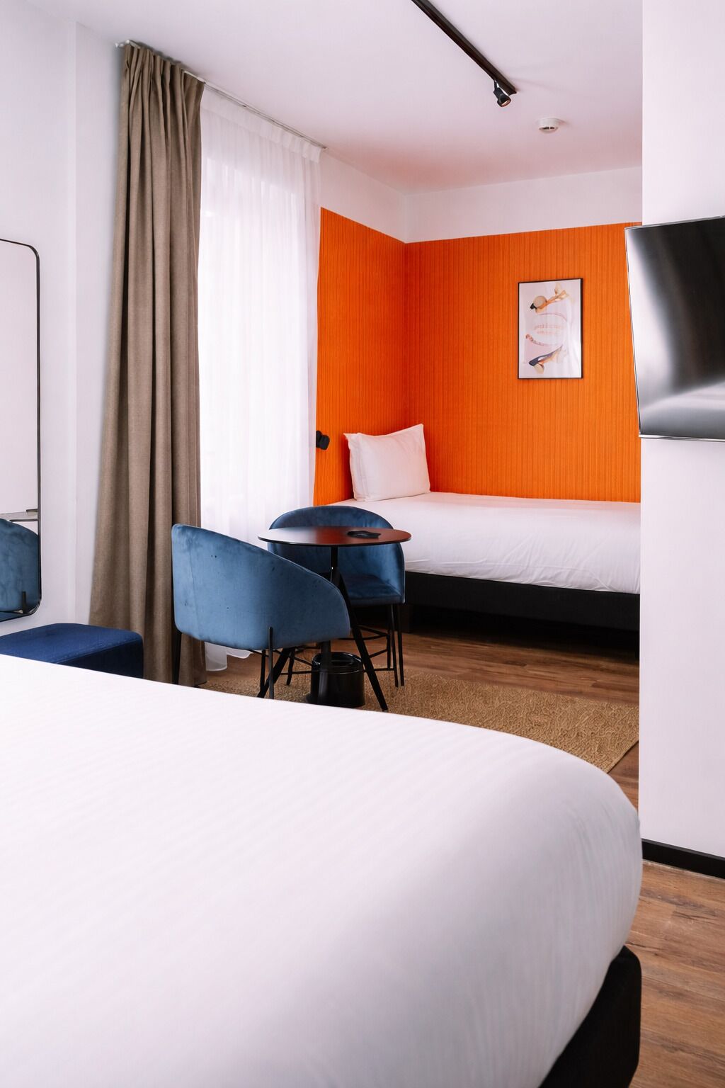 Une chambre d’hôtel avec un lit, un bureau, deux chaises, une télévision et une fenêtre avec des rideaux.