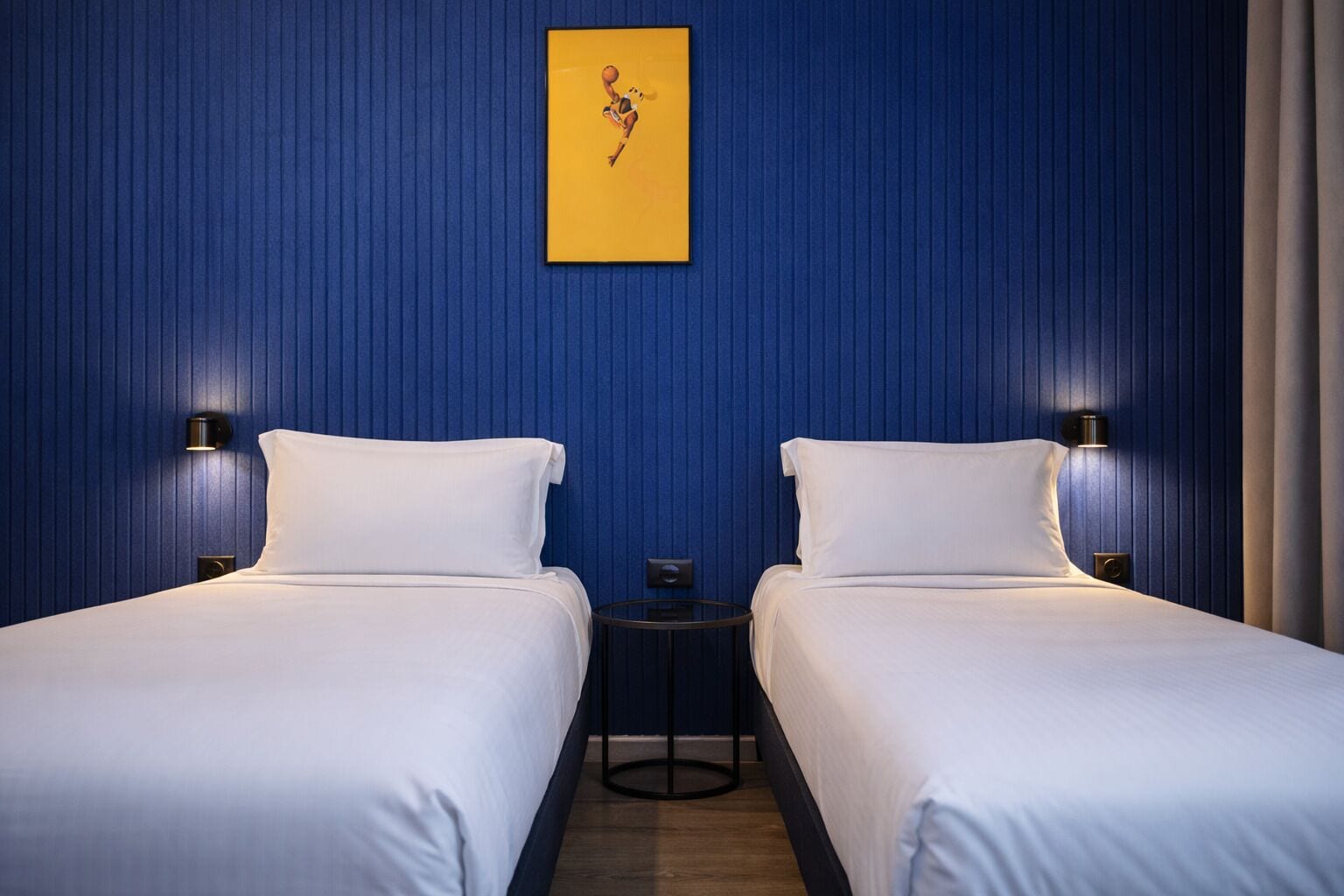 A hotel room with two beds, a small table, and a wall-mounted artwork.