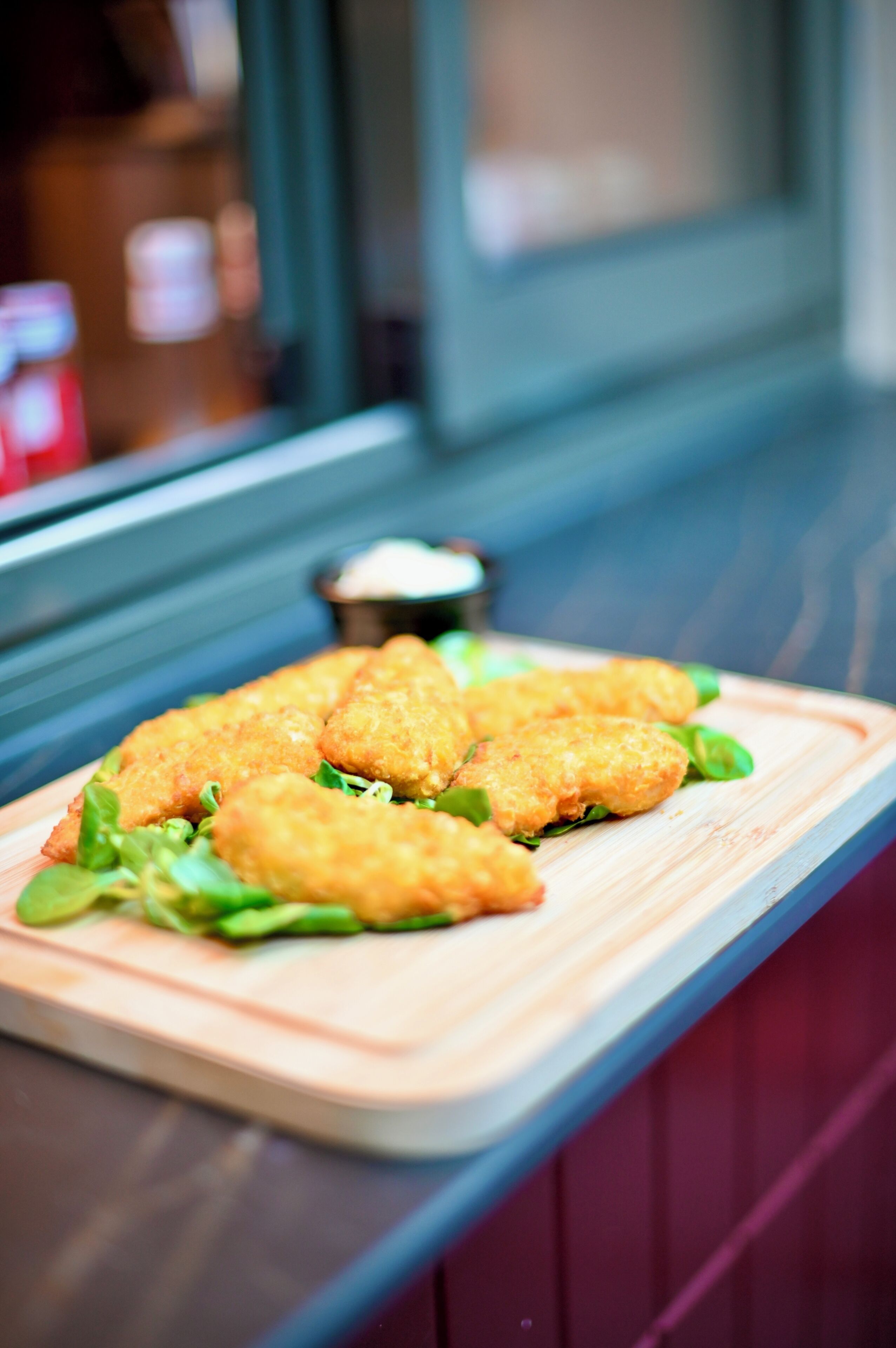 A wooden serving board with breaded food items and greens, placed on a counter.