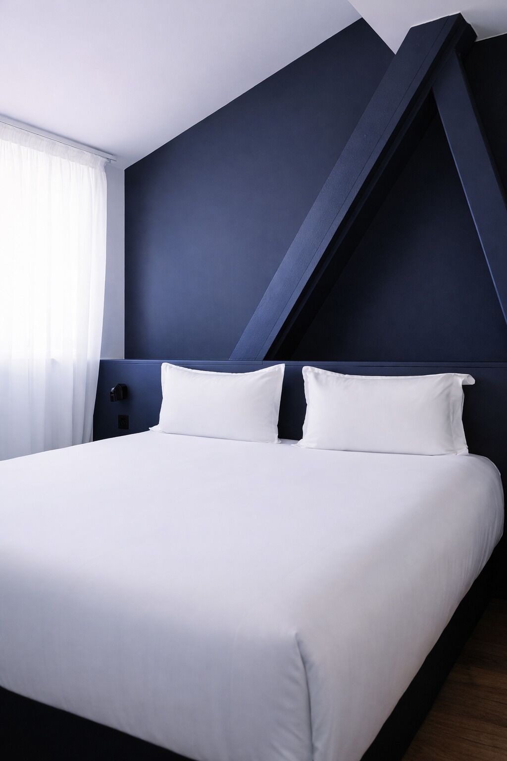 Una habitación de hotel moderna con una cama grande, paredes azul oscuro y techo inclinado.
