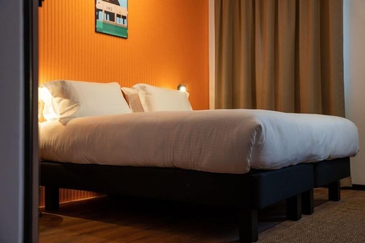 A bed with white bedding in a room with wooden flooring and a brown wall.