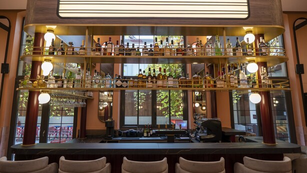 A bar with multiple shelves of bottles and glasses, a counter with a cash register, and bar stools. - ClapClap Hôtel Strasbourg (Strasbourg)