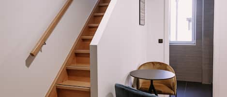 A staircase leading to a landing with a wooden finish, a small round table with a chair, and a door with a window view.