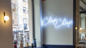 A cozy cafe interior with a neon sign reading "Clap Clap," comfortable seating, and a view of the street outside. - ClapClap Hôtel Strasbourg (Strasbourg)