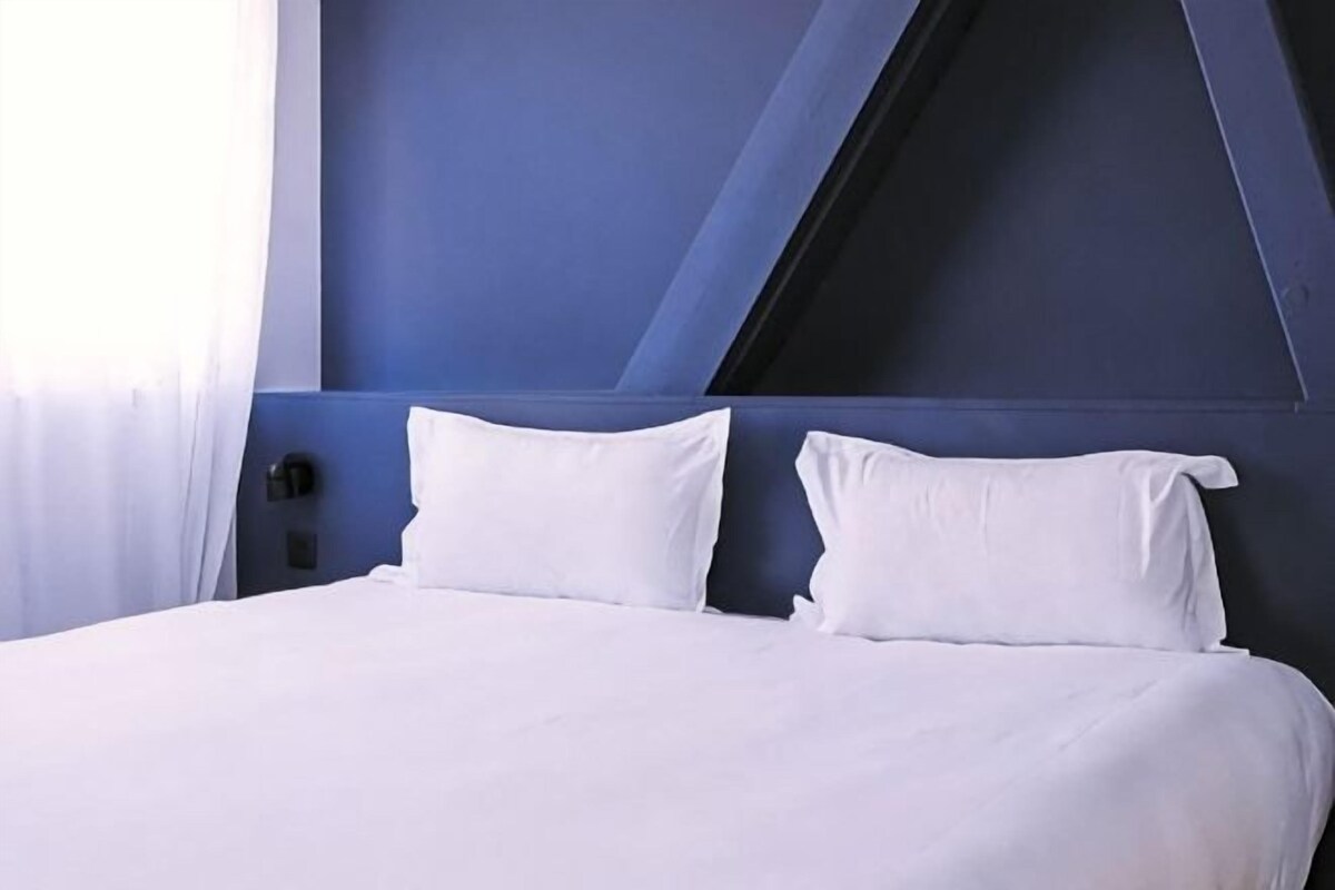 Un letto con lenzuola bianche, una testiera blu scuro e un cuscino bianco.