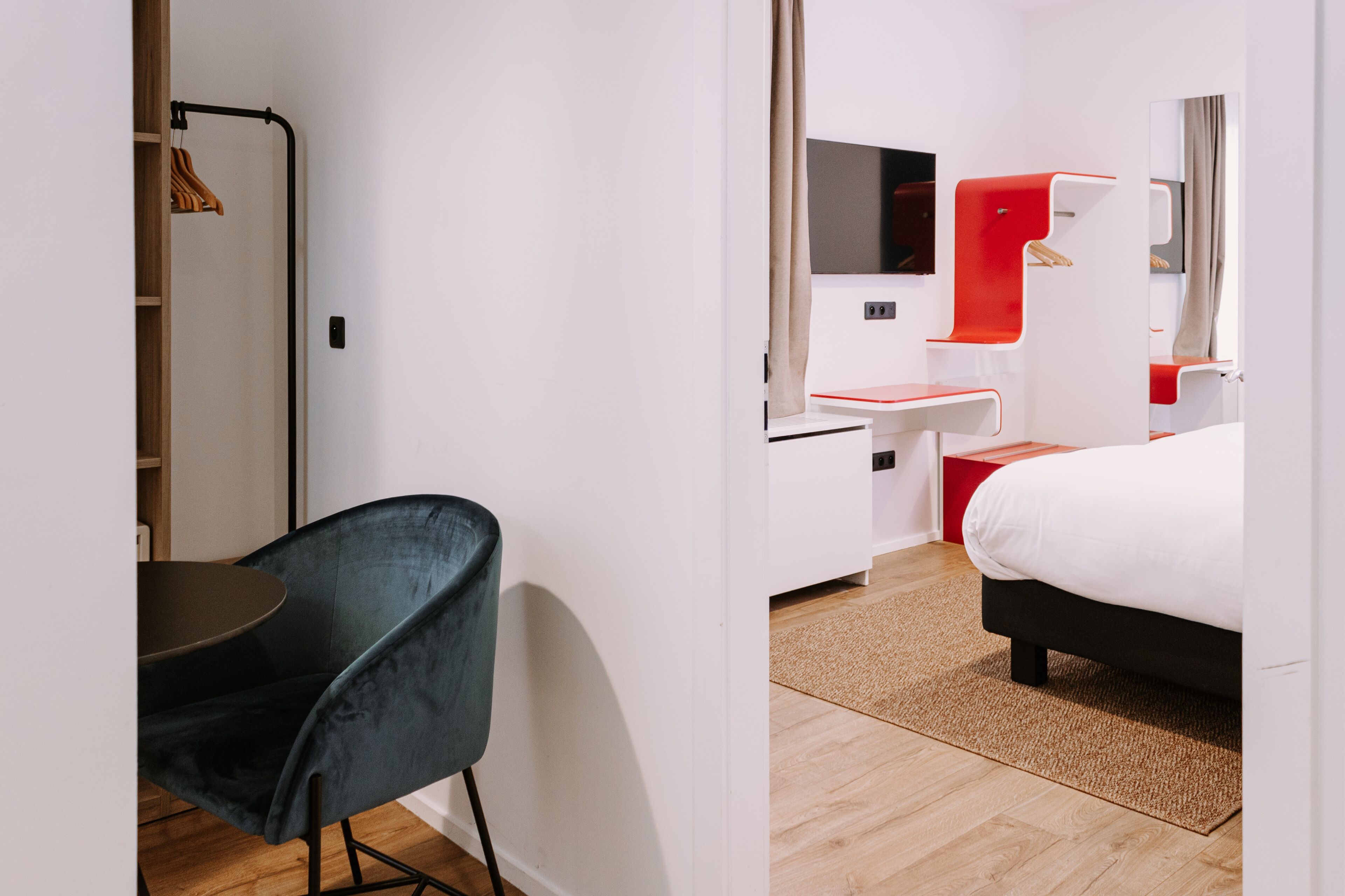 A modern hotel room with a bed, a desk, a chair, and a wardrobe.