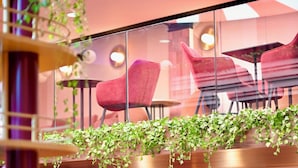 A restaurant with red chairs, round tables, and hanging plants. - ClapClap Hôtel Strasbourg (Strasbourg)