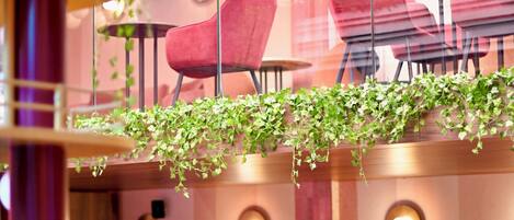 Un restaurant avec des chaises rouges, des tables rondes et des plantes suspendues.