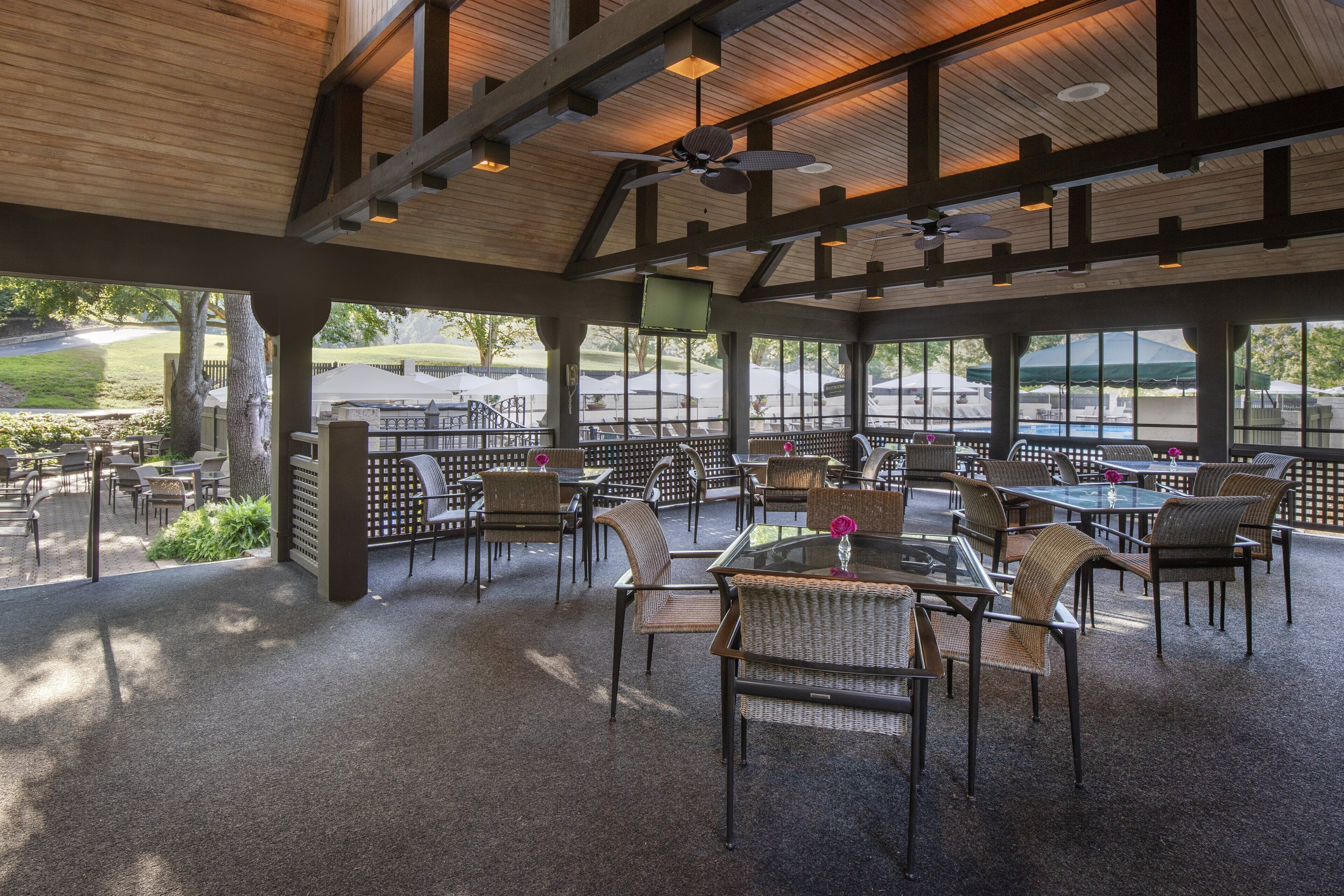 Eine Terrasse im Freien mit Tischen, Stühlen, einem Deckenventilator und Blick auf einen Golfplatz.