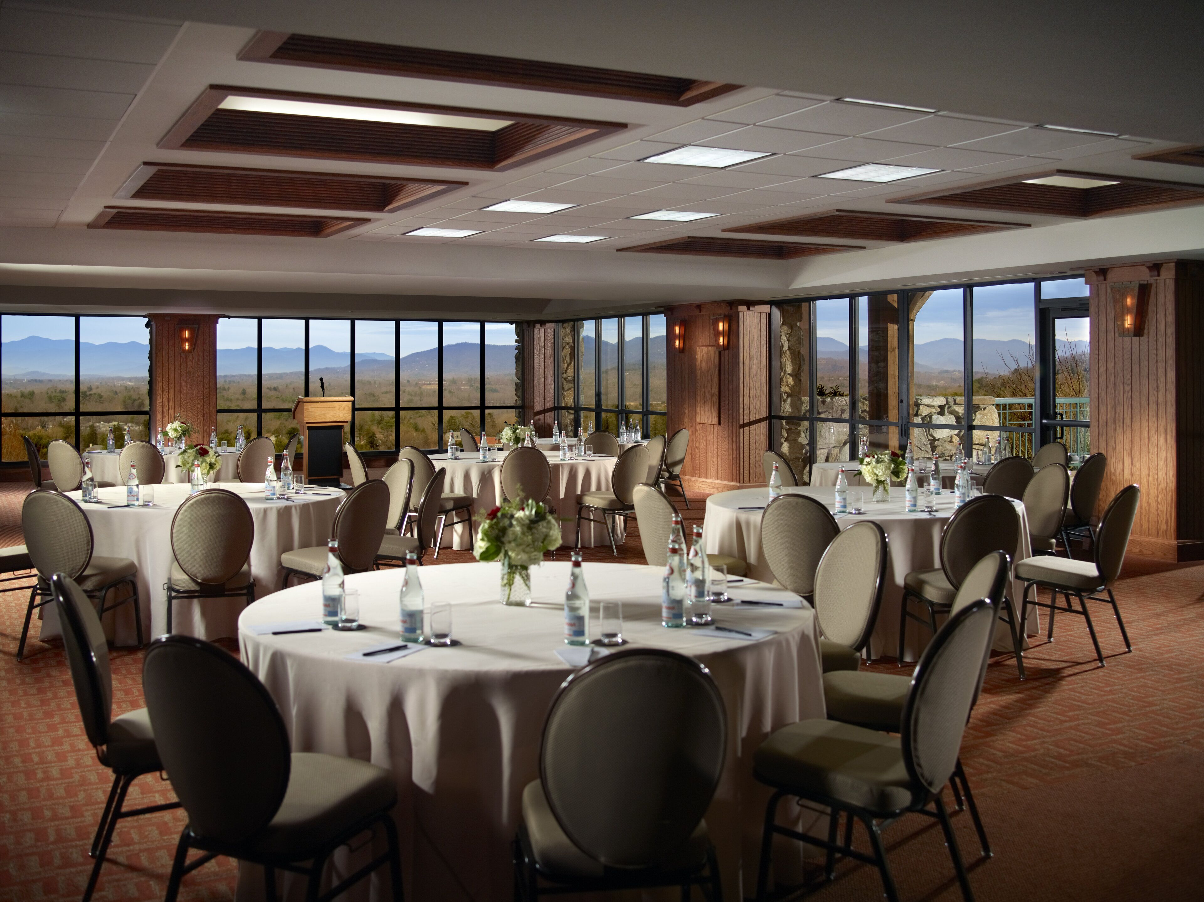 A conference room with round tables, chairs, and a large window offering a mountain view.