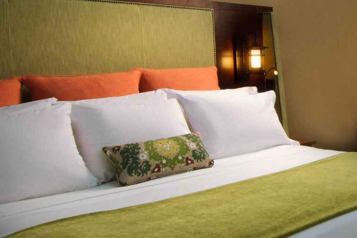 A neatly made bed with white and orange pillows, a green throw blanket, and a floral pillow.