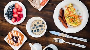 A breakfast table with various food items including toast, strawberries, blueberries, oatmeal, an omelet, bacon, and a croissant.