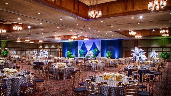 A banquet hall with round tables set for dining, a stage with floral decorations, and chandeliers. - The Omni Grove Park Inn & Spa (Asheville)