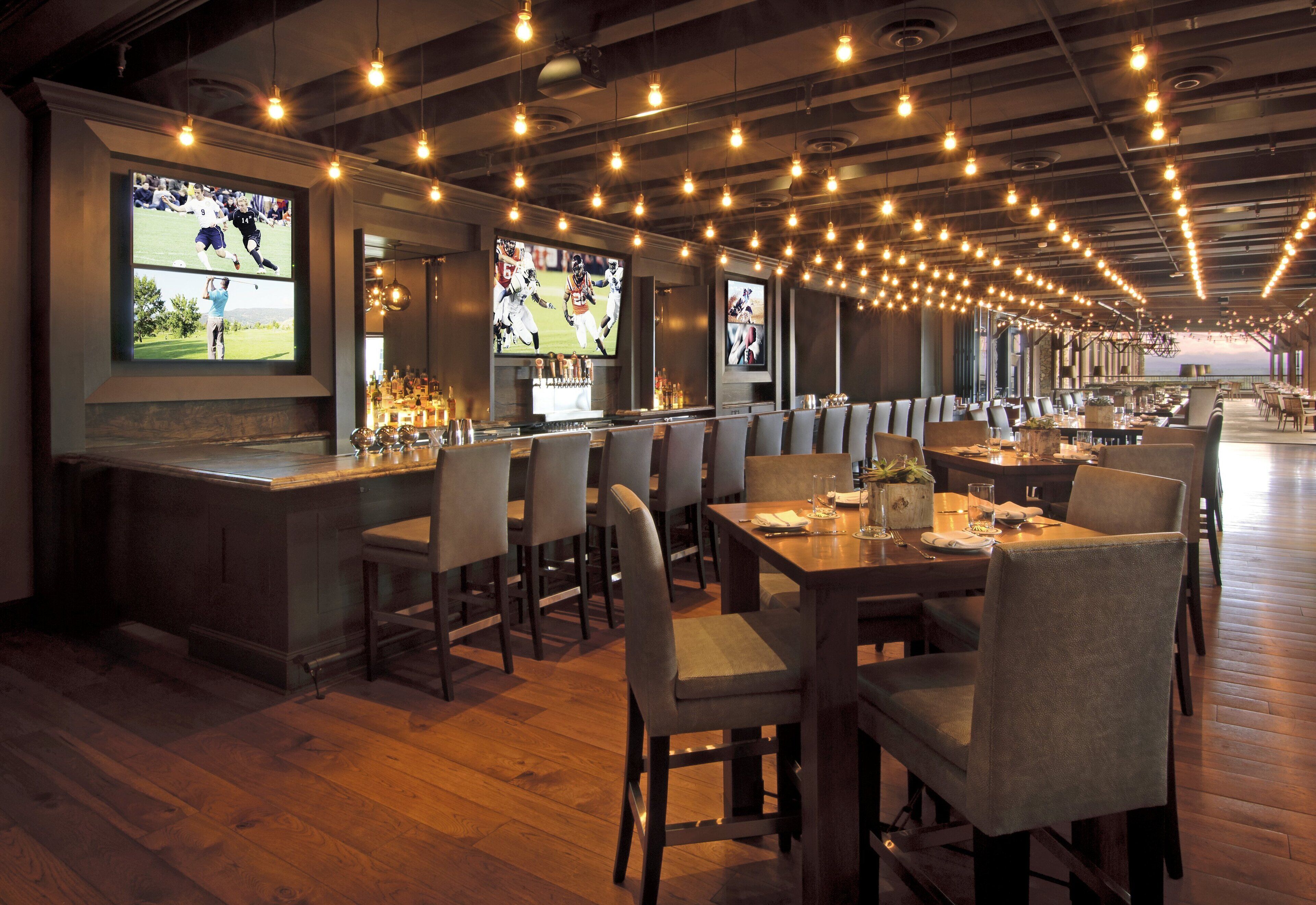 A restaurant with multiple seating areas, a bar, and large screens displaying sports events.