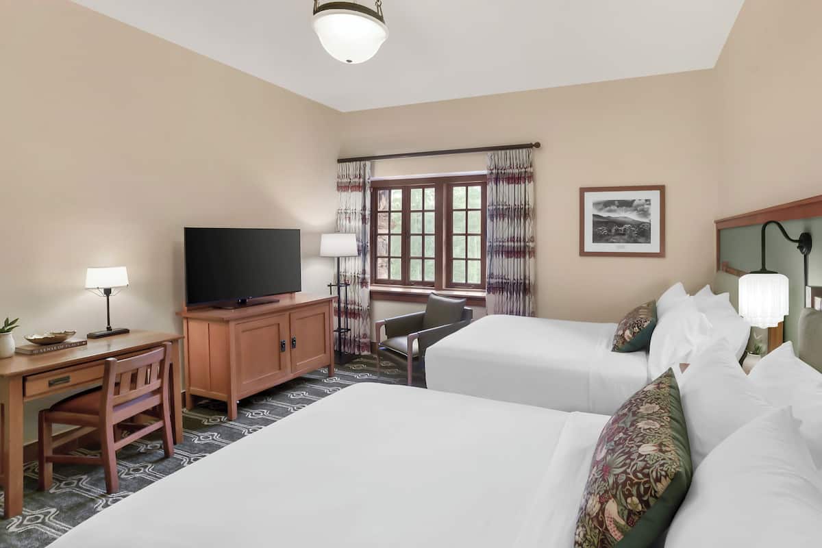 A hotel room with two beds, a desk with a TV, a chair, and a window with curtains.