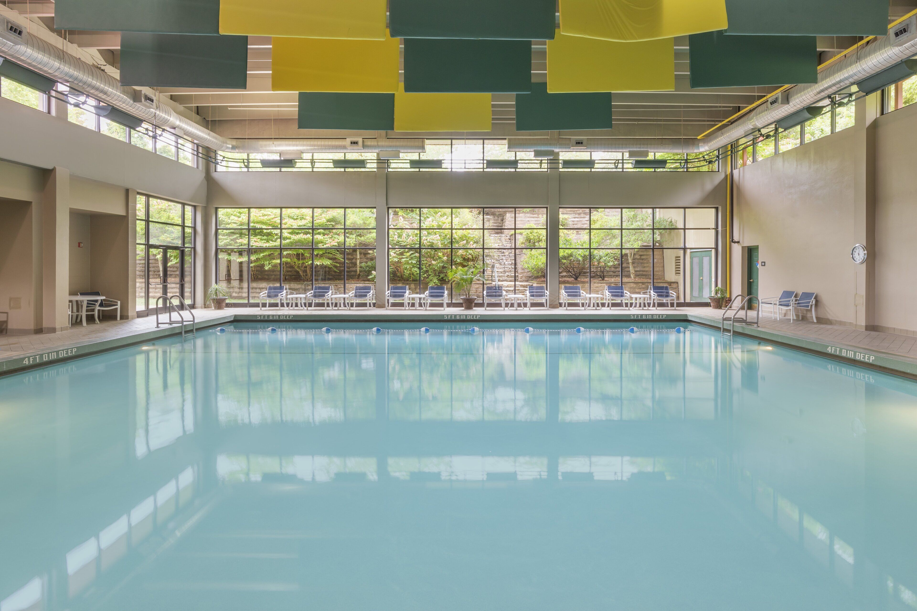 An indoor swimming pool with clear water, surrounded by windows and chairs.