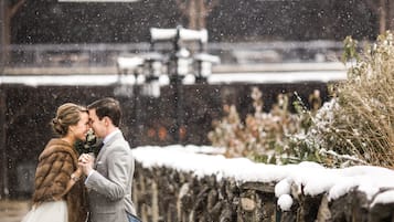 Una pareja se abraza en un entorno nevado al aire libre, con una valla de madera rústica y plantas cubiertas de nieve.