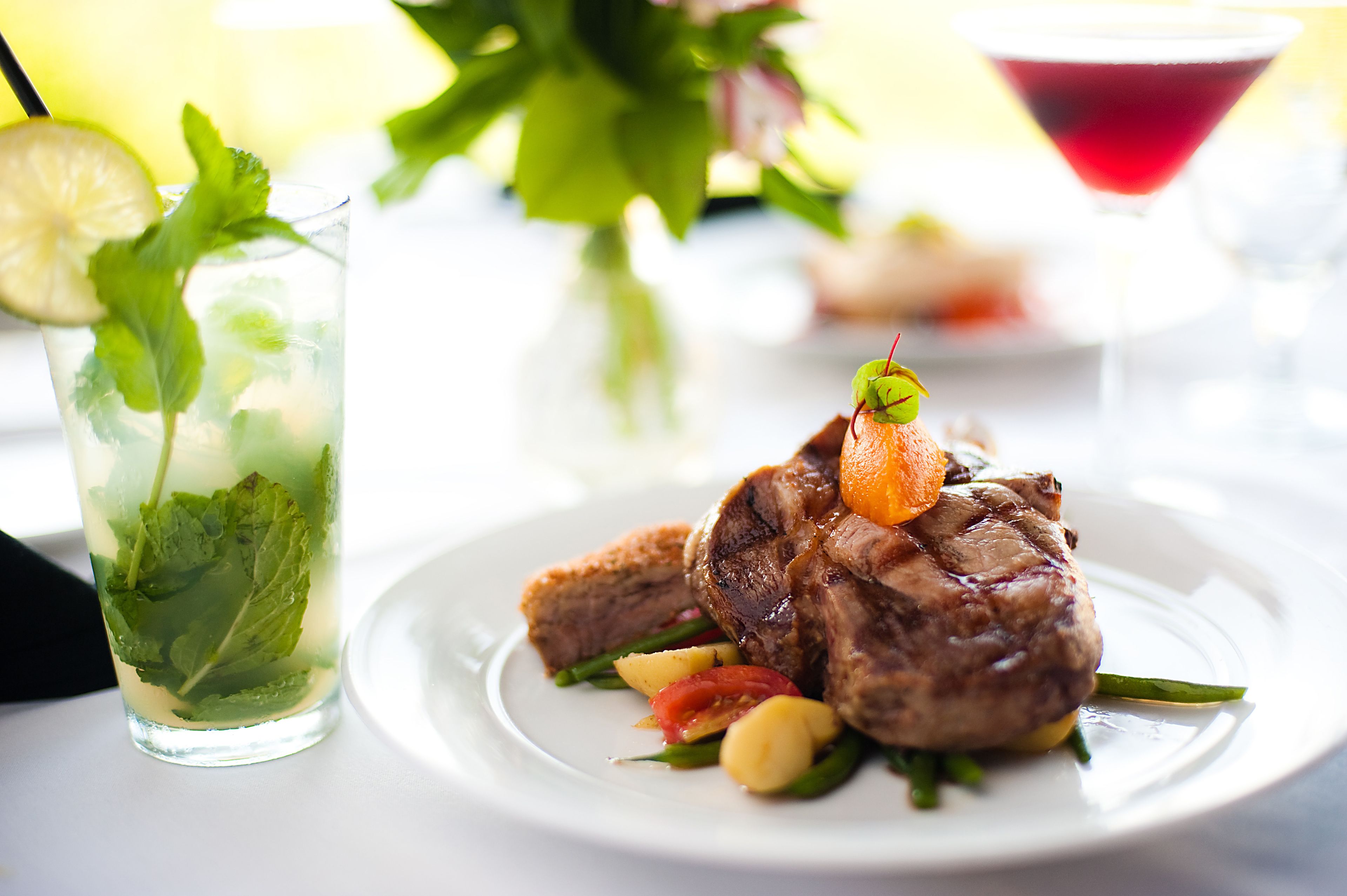 A plate of food with a glass of drink and a martini glass in the background.
