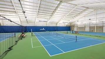 An indoor tennis court with a net, benches, and a banner.
