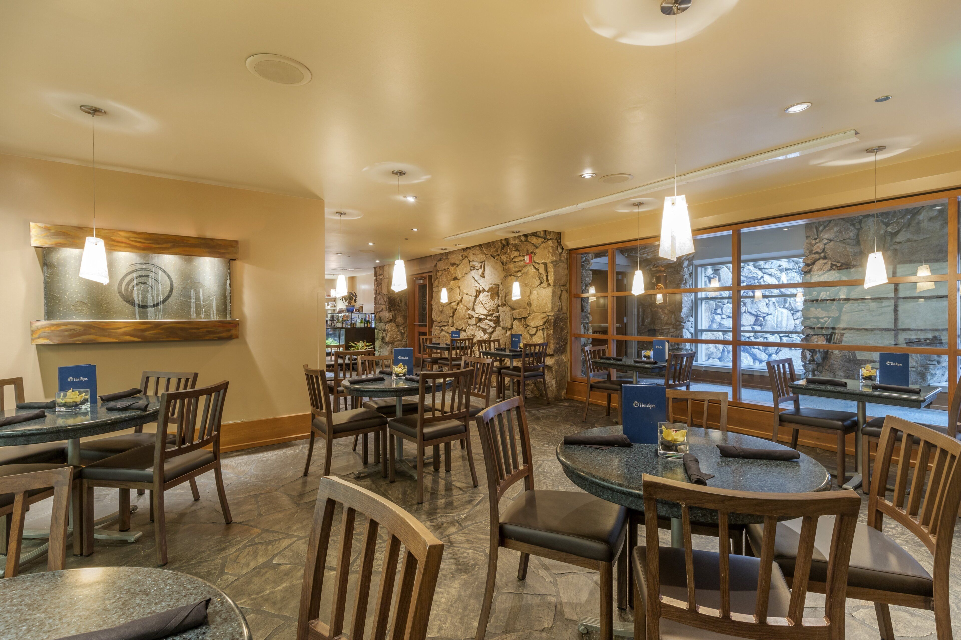 A restaurant with multiple tables and chairs, stone walls, and hanging pendant lights.