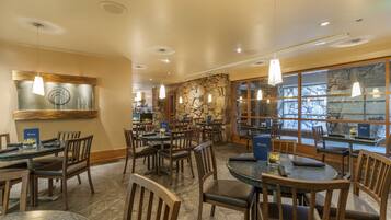 A restaurant with multiple tables and chairs, stone walls, and hanging pendant lights.
