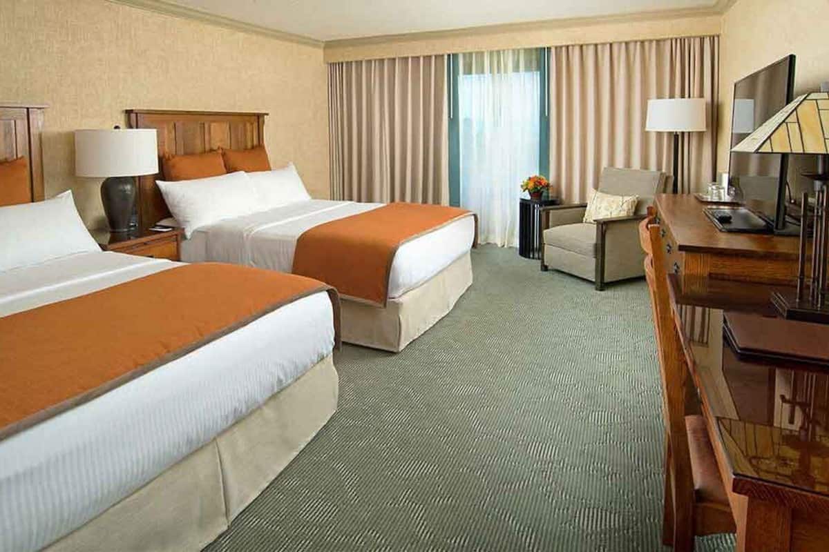 A hotel room with two beds, a desk, a chair, and a television.