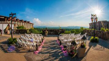 An outdoor wedding venue with white chairs arranged in rows, stone walls, and a view of distant mountains.