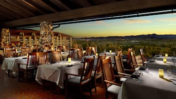 A restaurant with tables set for dining, overlooking a scenic view of mountains and a city skyline.
