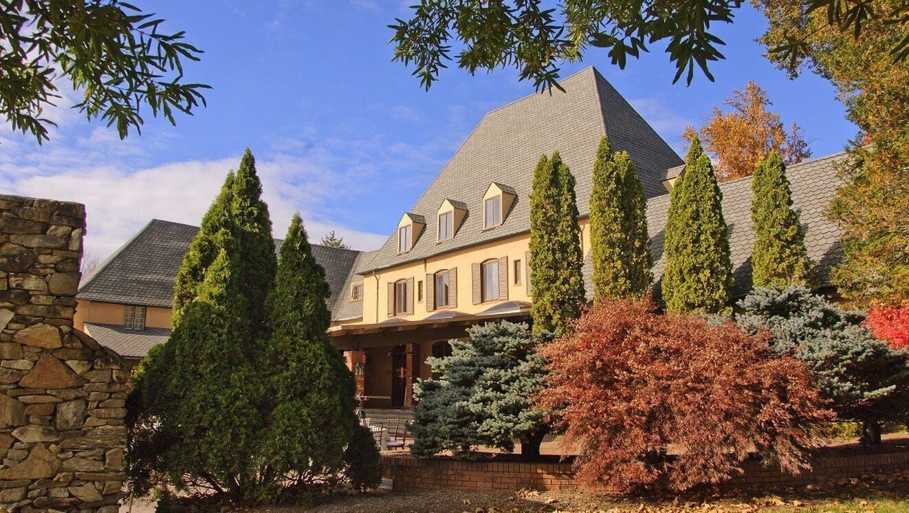 A large house with a stone wall, multiple trees, and a clear sky.