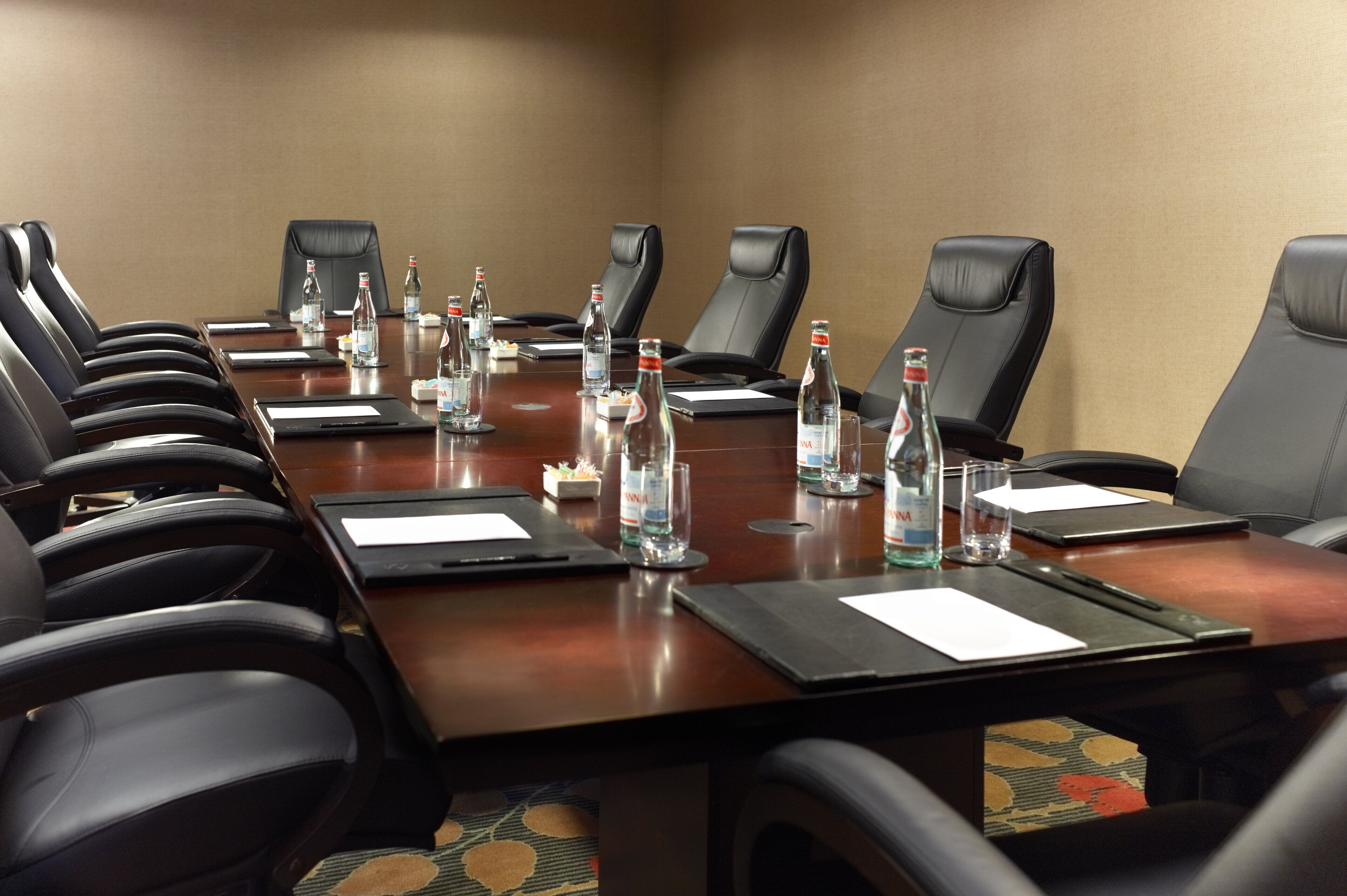 A conference room with a long table, black leather chairs, water bottles, and nameplates.