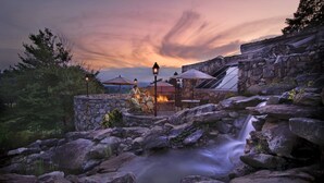 A stone-walled outdoor area with a small waterfall, stone seating, and umbrellas. - The Omni Grove Park Inn & Spa (Asheville)