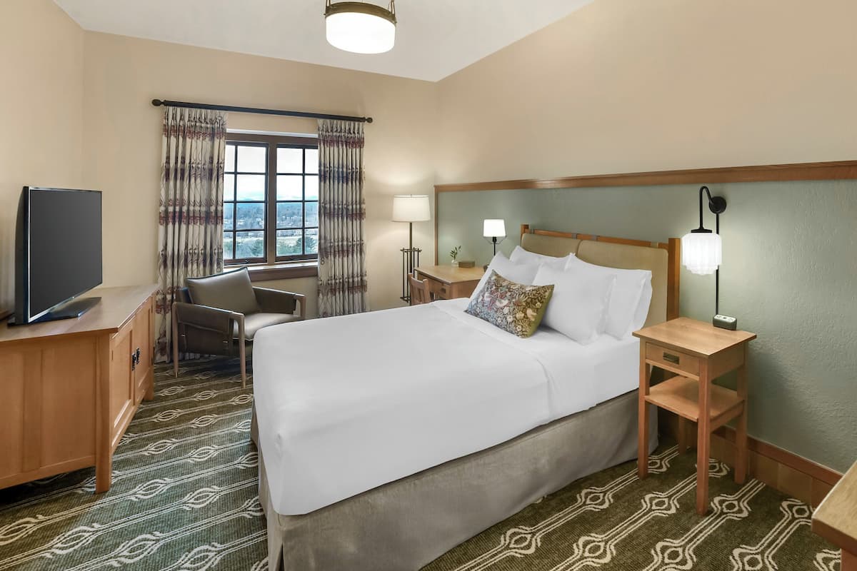A hotel room with a large bed, a desk, a chair, a television, and a window with curtains.