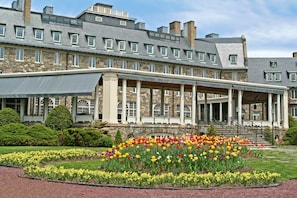 Un gran edificio de piedra con un porche cubierto y un jardín lleno de flores coloridas.