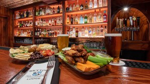 A bar area with a variety of liquor bottles, a tray of food including wings and vegetables, and a glass of beer. - Skytop Lodge (Skytop)