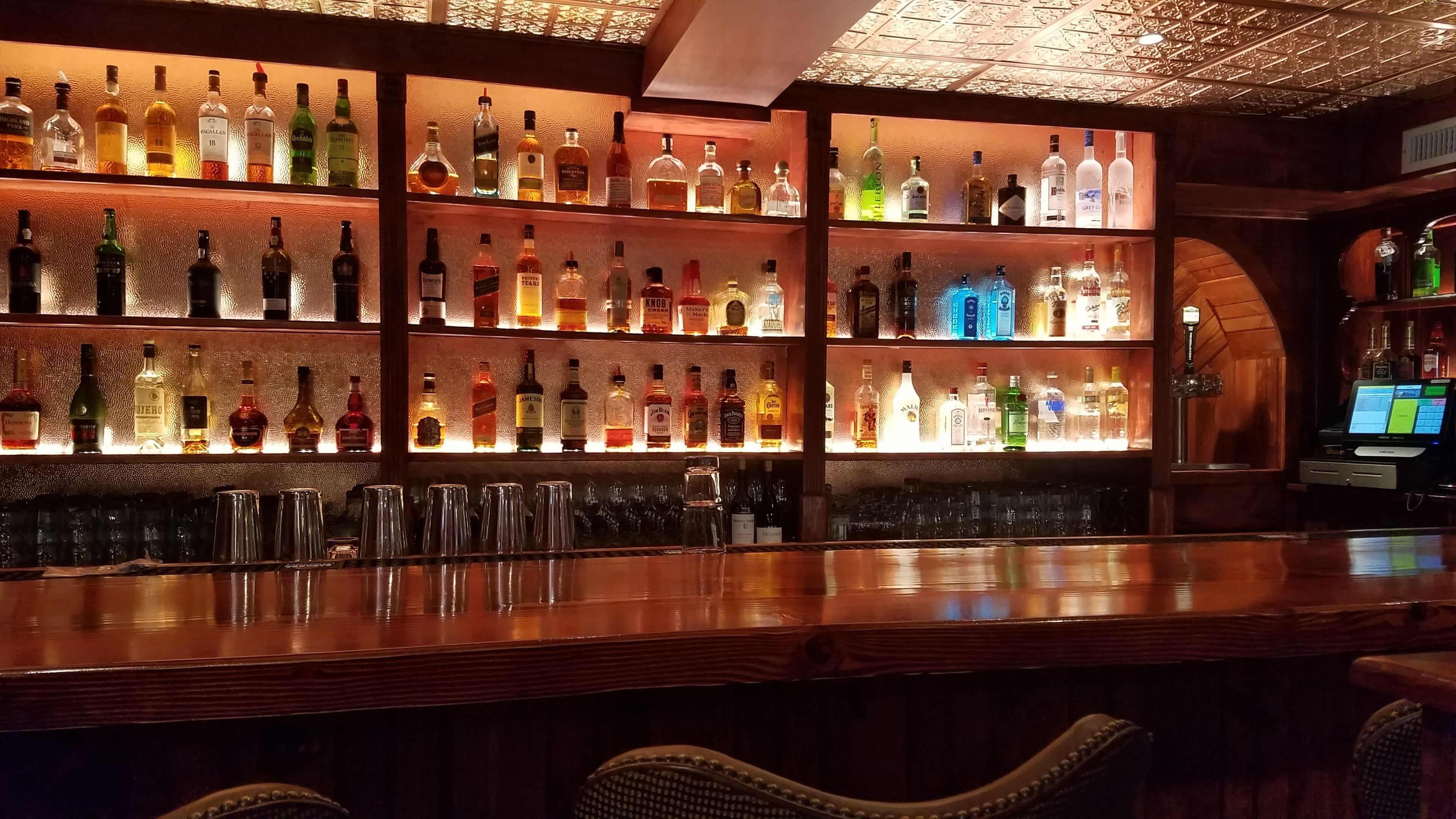 A bar area with multiple shelves of liquor bottles and glasses.