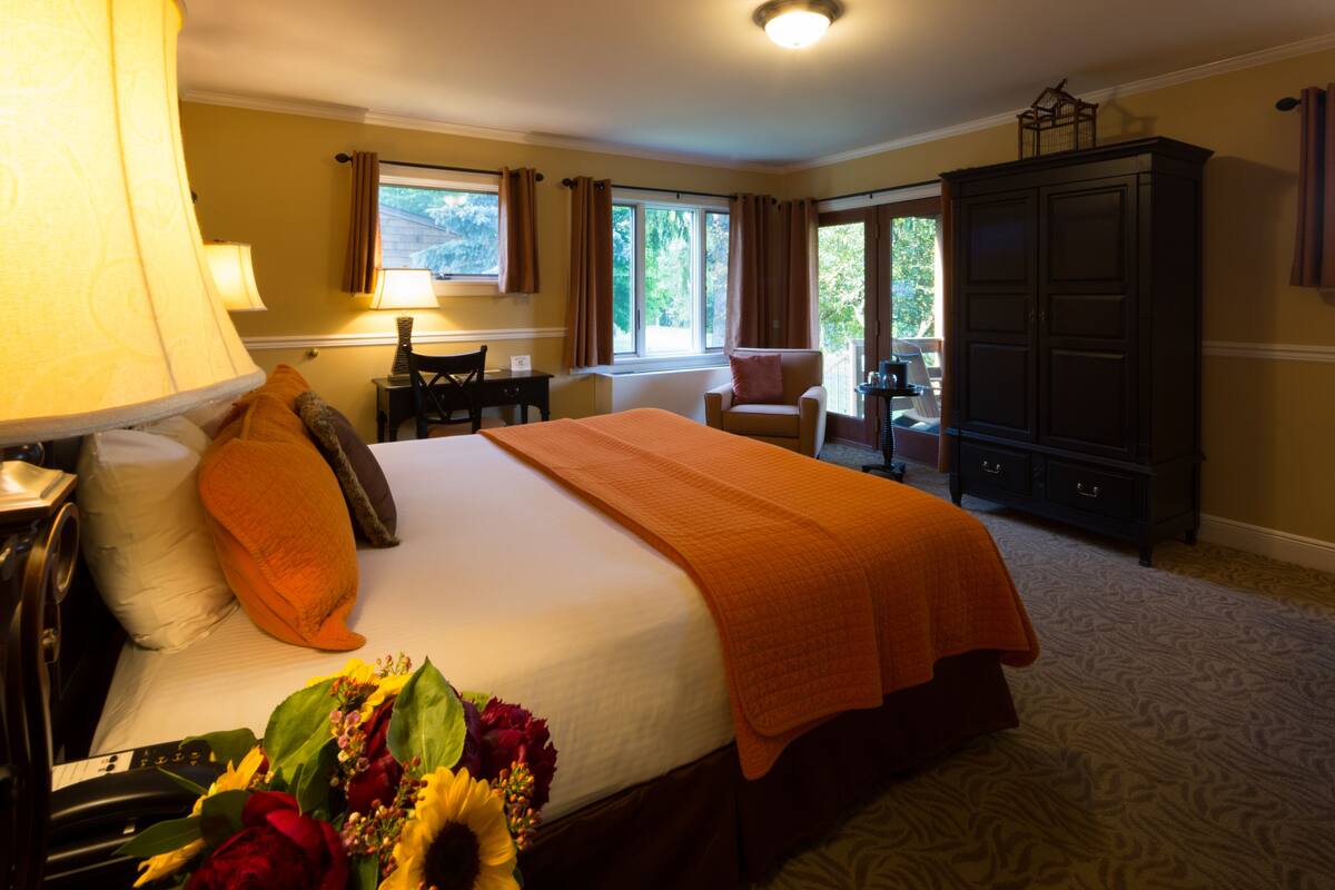 A hotel room with a bed, a desk, a chair, a wardrobe, and a view of the outdoors.