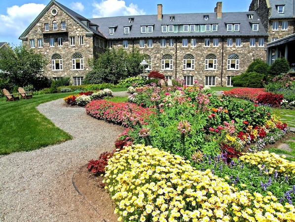 A stone building with multiple windows and a garden with colorful flowers.