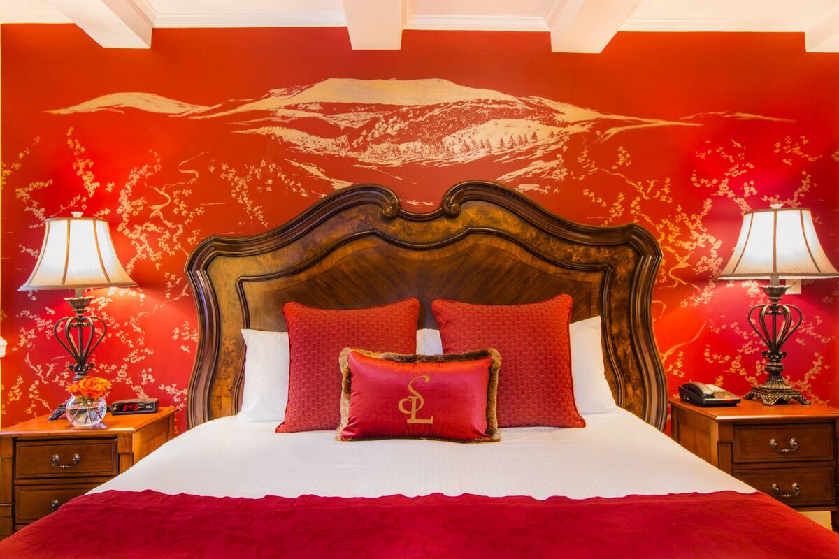 A bed with a wooden headboard, red bedding, and two bedside tables with lamps.