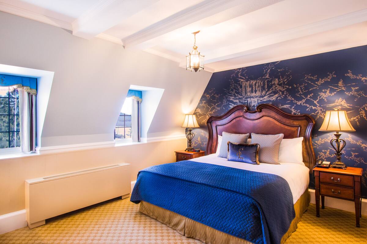A bedroom with a large bed, two bedside tables with lamps, a radiator, and a window with curtains.