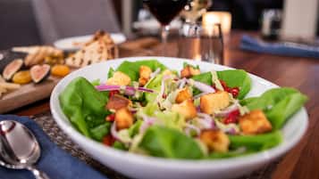 A plate of salad with croutons and red onion, accompanied by a glass of red wine and a candle on a table.