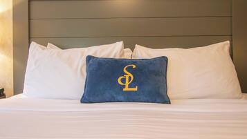 A bed with white bedding and a single blue pillow with a gold letter 'S' on a dark headboard.