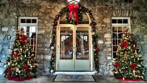 A stone building entrance with a Christmas tree on each side and a wreath above the door. - Skytop Lodge (Skytop)