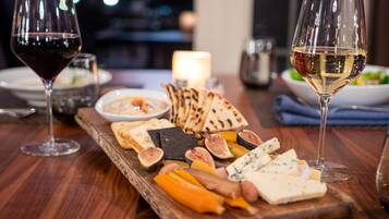 A wooden board with various cheeses, fruits, and crackers, accompanied by two wine glasses on a wooden table.