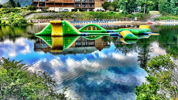 A lakeside view with a large house, a reflection of colorful inflatable slides, and a clear sky. - Skytop Lodge (Skytop)