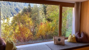 Asiento junto a la ventana con vista a follaje otoñal, un banco de madera y una bolsa con la etiqueta "SALADINA".