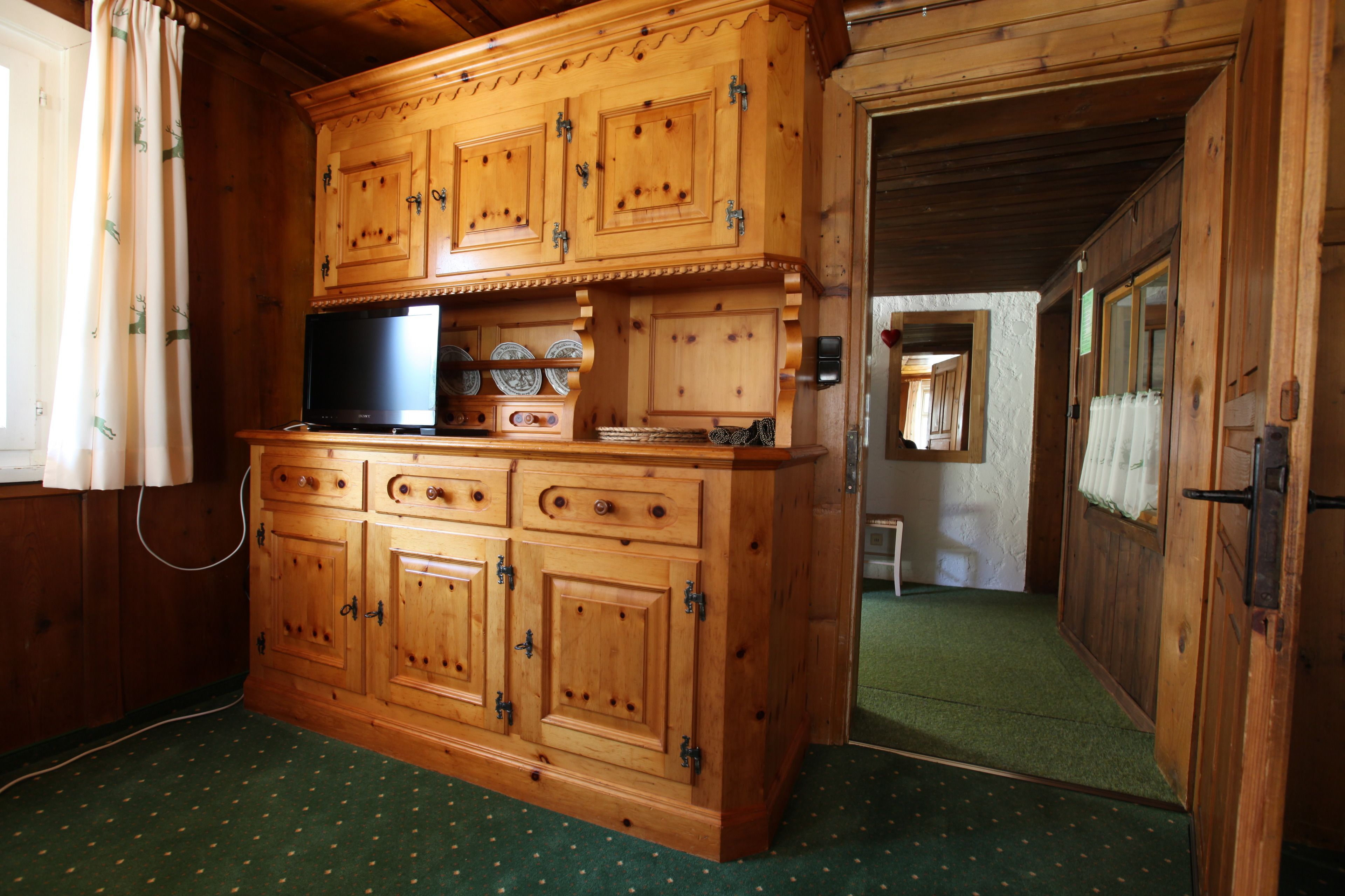 Eine Holzkabine mit einem Flachbildfernseher, Schubladen und einem Regal mit dekorativen Tellern.