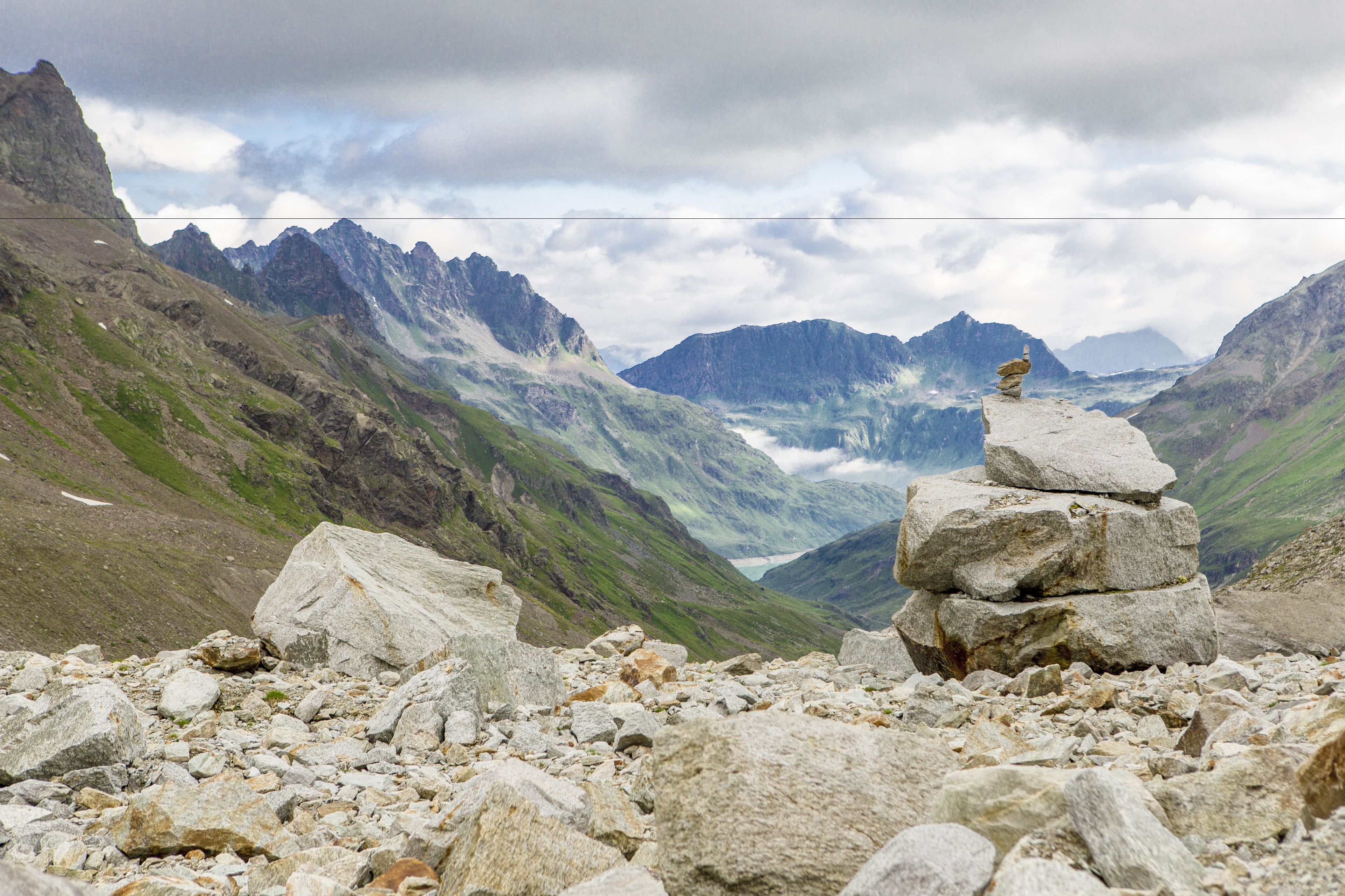 Eine gebirgige Landschaft mit einem Felsensturz im Vordergrund und einem Tal mit einem Gletscher im Hintergrund.